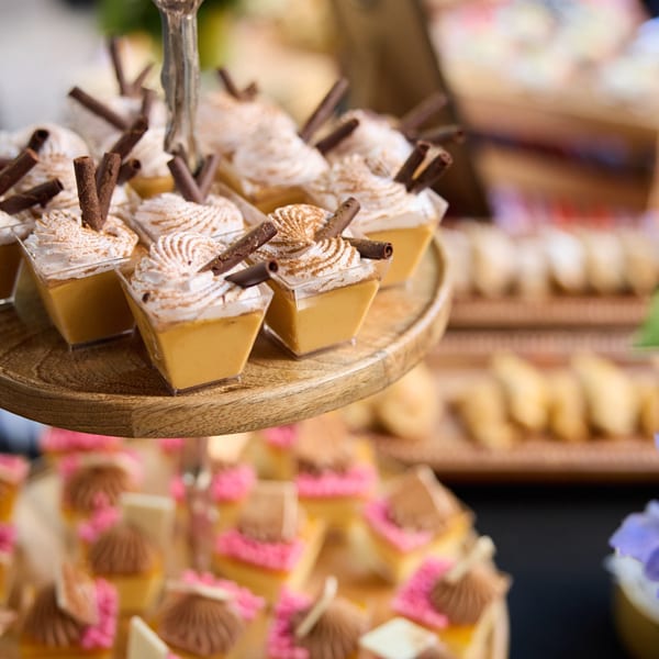 Mini dessert cups with whipped cream, cinnamon, and chocolate sticks on a tiered wooden tray.