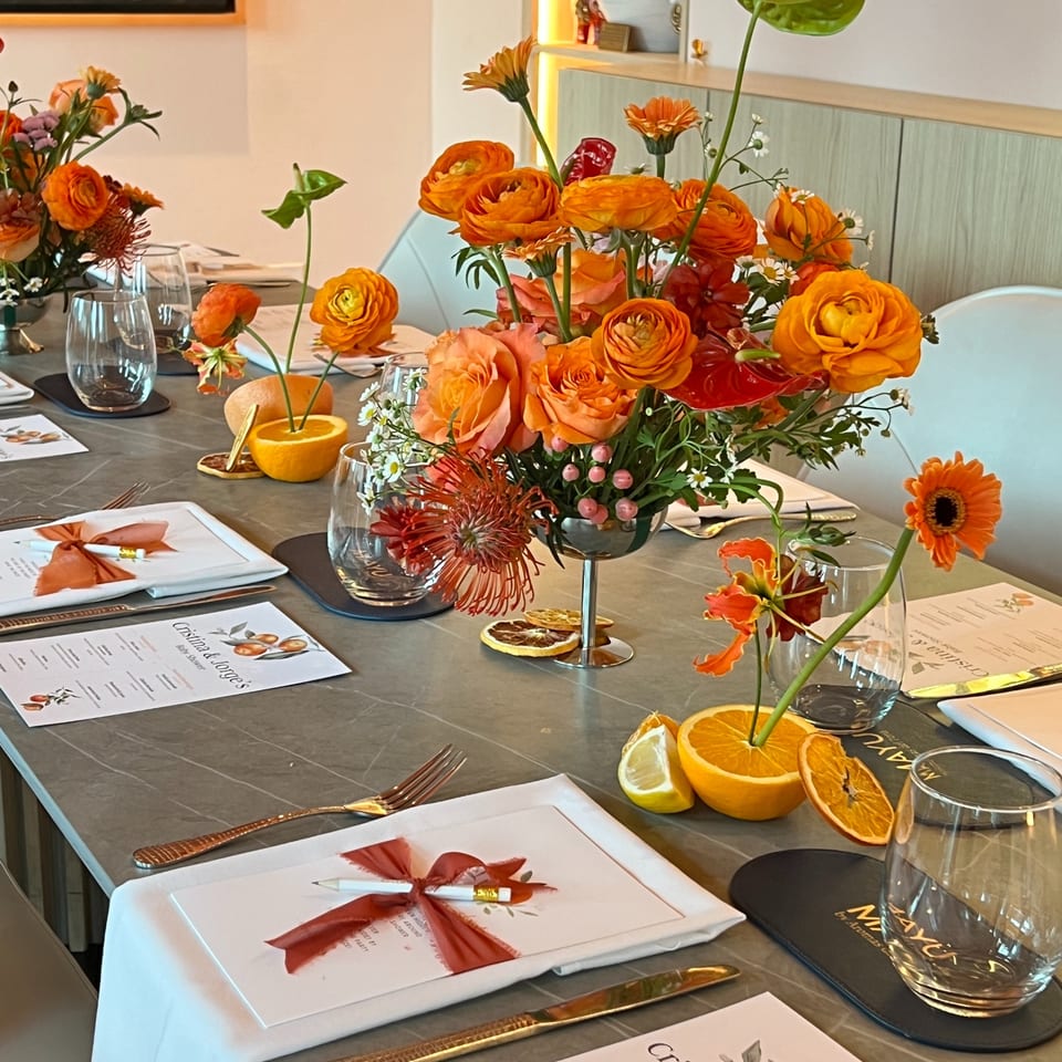 Table set for a baby shower with orange floral centerpieces, menus, and place settings.