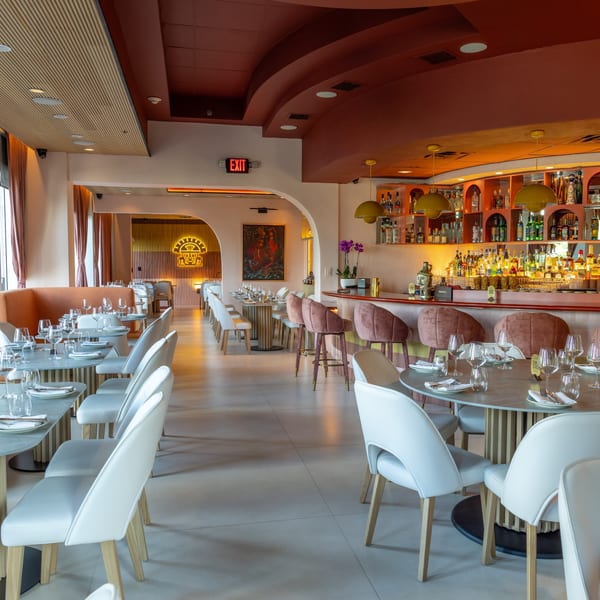 A modern restaurant interior with set tables, a bar with stools, and warm lighting.