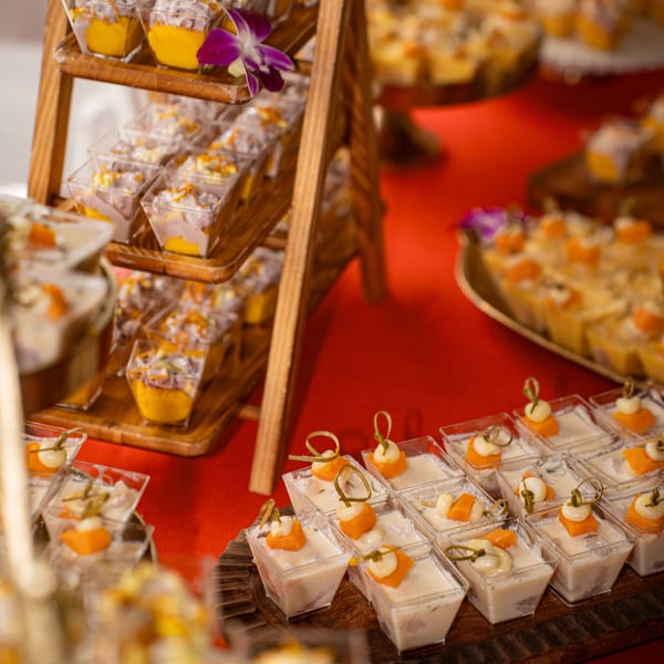 Dessert display with small square cups of layered mango and cream desserts on a red tablecloth.
