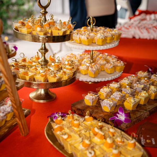 A vibrant dessert spread with mango and taro puddings in small cups on tiered stands and wooden boards.