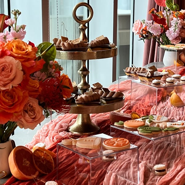 A dessert table with chocolate treats, decorated cookies, and fresh flowers on pink and red draped fabric.