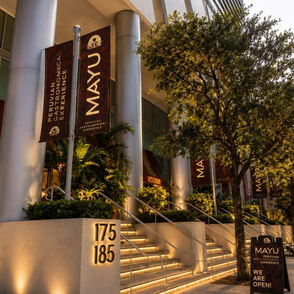 Exterior of Mayu Peruvian restaurant with illuminated steps, banners, and an "OPEN" sign.