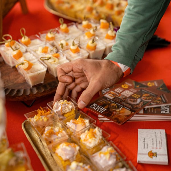 A hand reaches for a small dessert cup from a tray of appetizers on a red tablecloth.