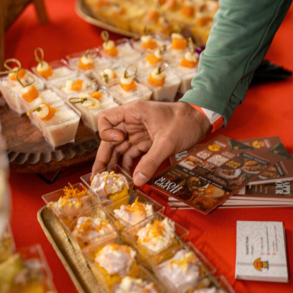 A hand reaches for a small dessert cup from a tray of appetizers on a red tablecloth.