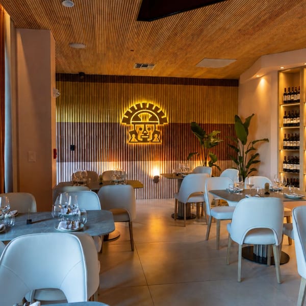 Modern restaurant interior with white chairs, set tables, a glowing logo, and a wine display.